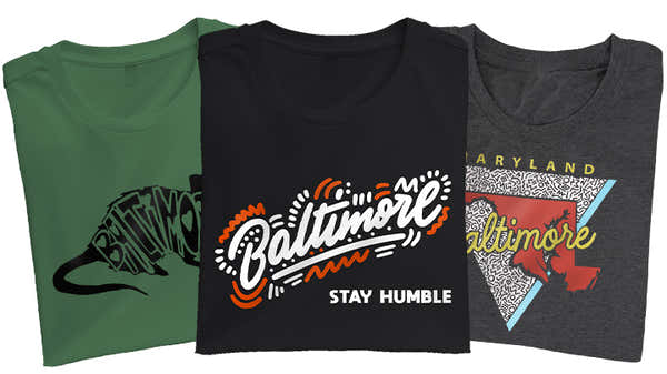 A collection of Baltimore-inspired T-shirts in green, blue, and gray, each featuring creative designs that celebrate the iconic city and its culture.