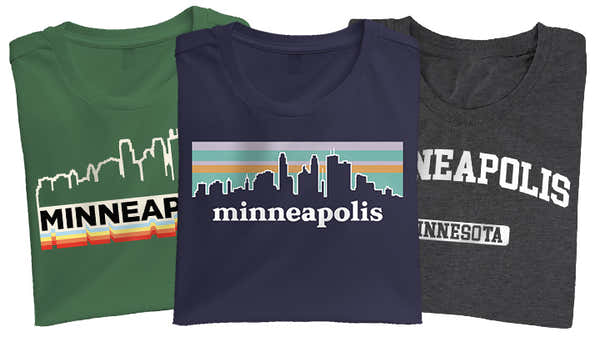 Three Minneapolis-themed t-shirts; green with a white skyline and 'MINNEAPOLIS' over sunset stripes, navy with 'minneapolis' and skyline in pastel colors, and charcoal with 'MINNEAPOLIS MINNESOTA' in white block letters.