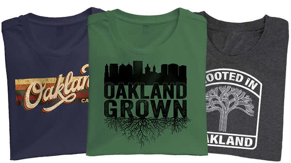 Three t-shirts laid out left to right with a navy one featuring an OAKLAND cursive designs, a green t-shirt feature an OAKLAND GROWN black design and a heather grey t-shirt with a white ROOTED IN OAKLAND t-shirt.