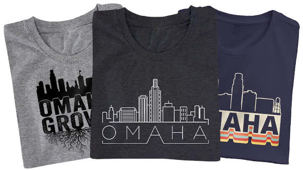 Banner displaying three folded t-shirts with 'OMAHA' designs: a black skyline with roots, a grey linear city outline, and a navy shirt with a retro striped pattern, from the 'Omaha' collection.