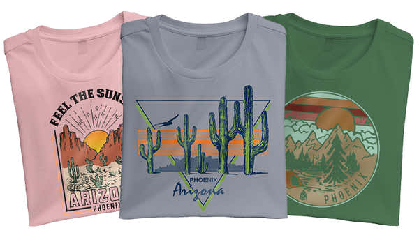 Banner with three folded t-shirts featuring Phoenix, Arizona designs: a pink one with a sunset and cactus, a grey one with a desert skyline, and a green one with a camping scene.