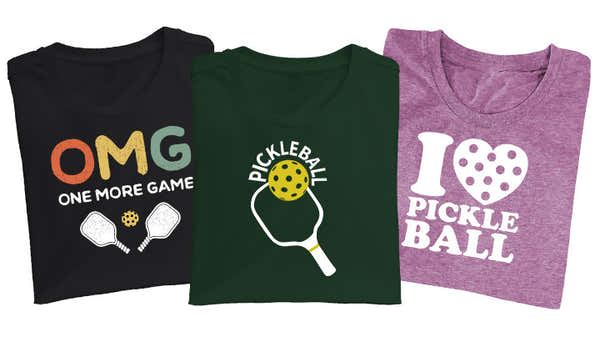 Three t-shirts with pickleball designs: one black with "OMG One More Game," one green with "Pickleball" and a paddle graphic, and one purple with "I (heart) Pickleball.  pen_spark