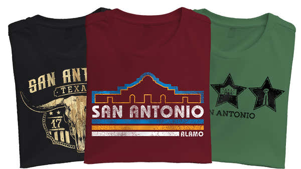 Banner with three folded t-shirts showcasing San Antonio: black with a longhorn skull, maroon with 'San Antonio Alamo' in western font, and green with star-shaped mission silhouettes.