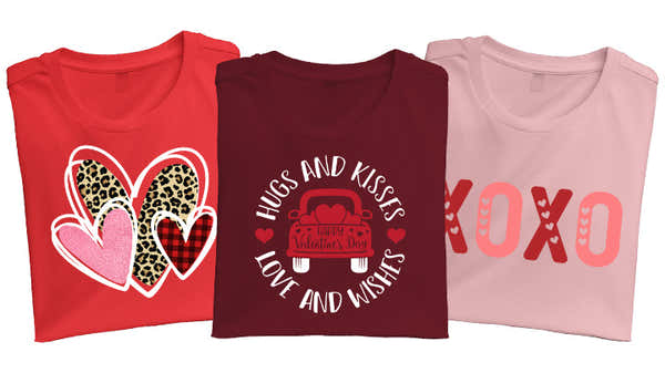 Three t-shirts laid out left to right with a red t-shirt with three hearts on it, a maroon t-shirt with a car design that says "hugs and kisses love and wishes" and a pink t-shirt with the design "XOXO."